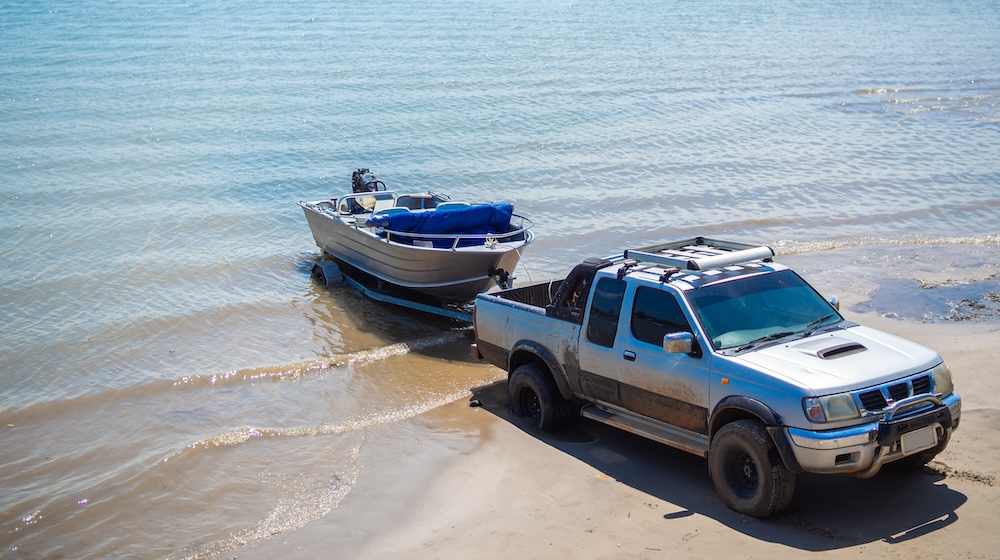Motor boat being pulled with the pickup truck trailer on the beach